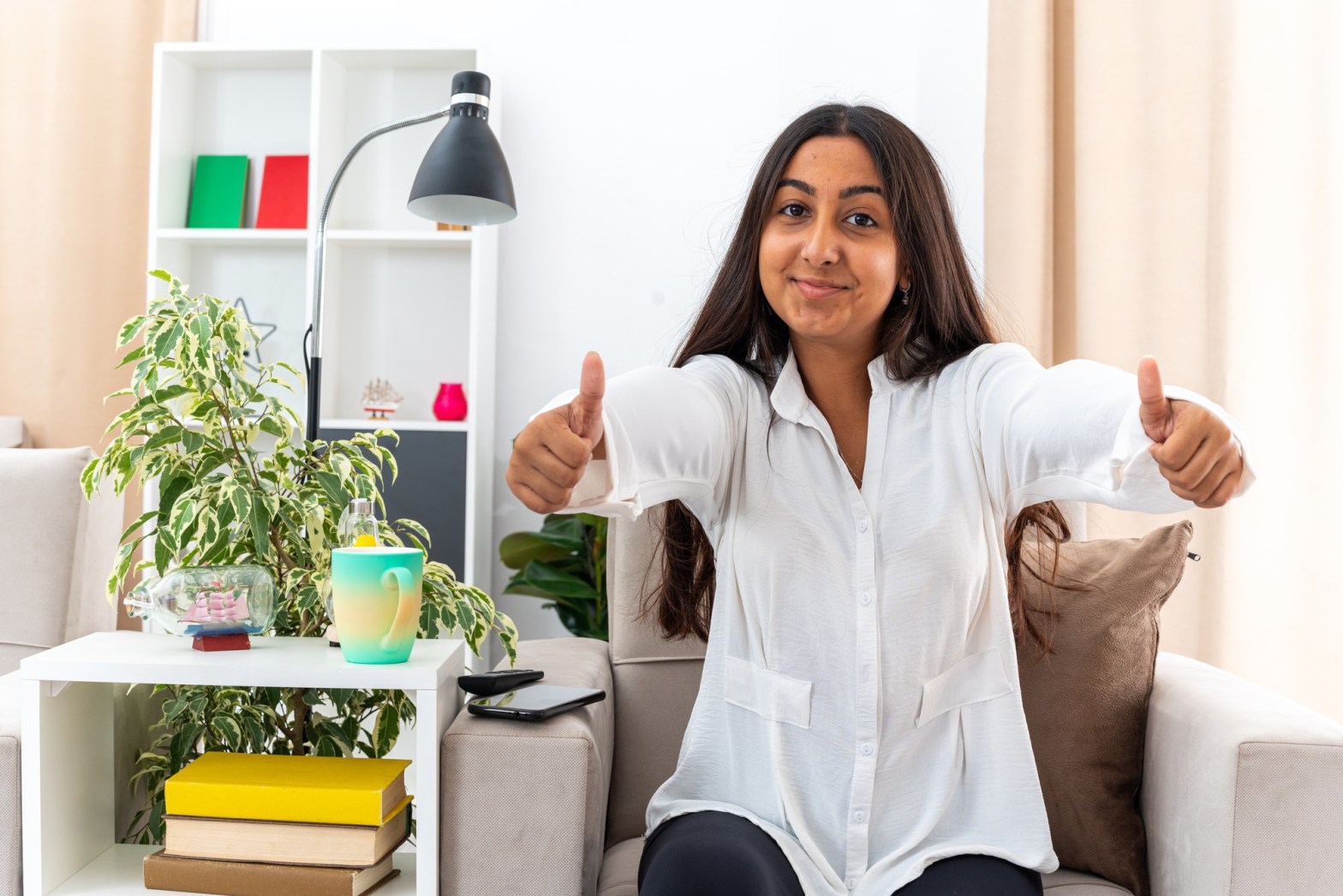 woman sitting on sofa giving thumbs up in bright living room   dr krishna athal