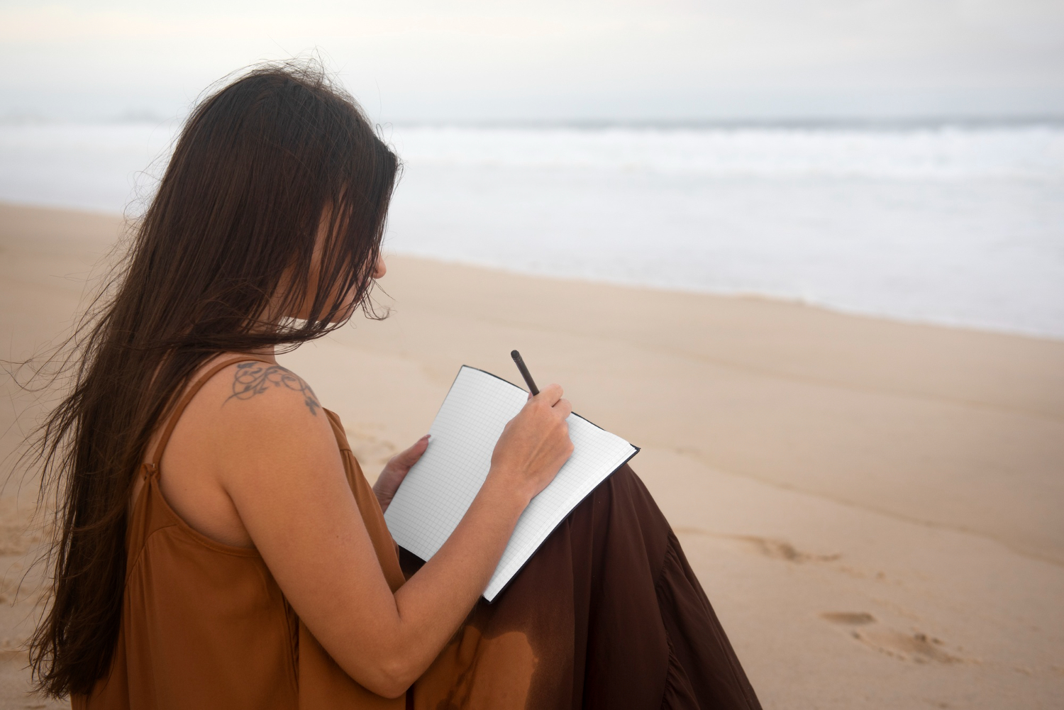woman writing in notebook on the beach by the sea   dr krishna athal
