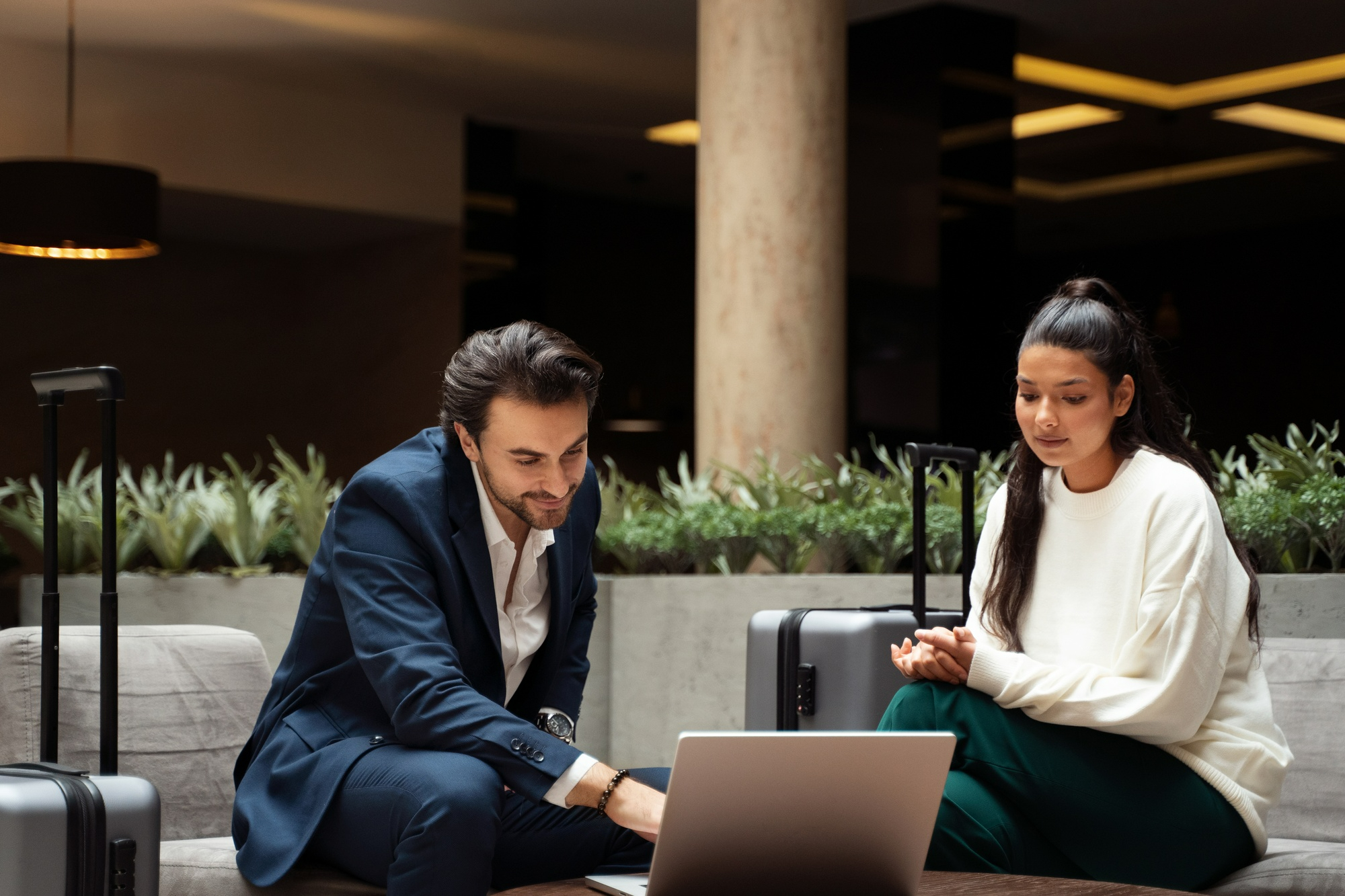 business mentor shows a professional woman something on a laptop in a modern hotel lobby with suitcases beside them   dr krishna athal